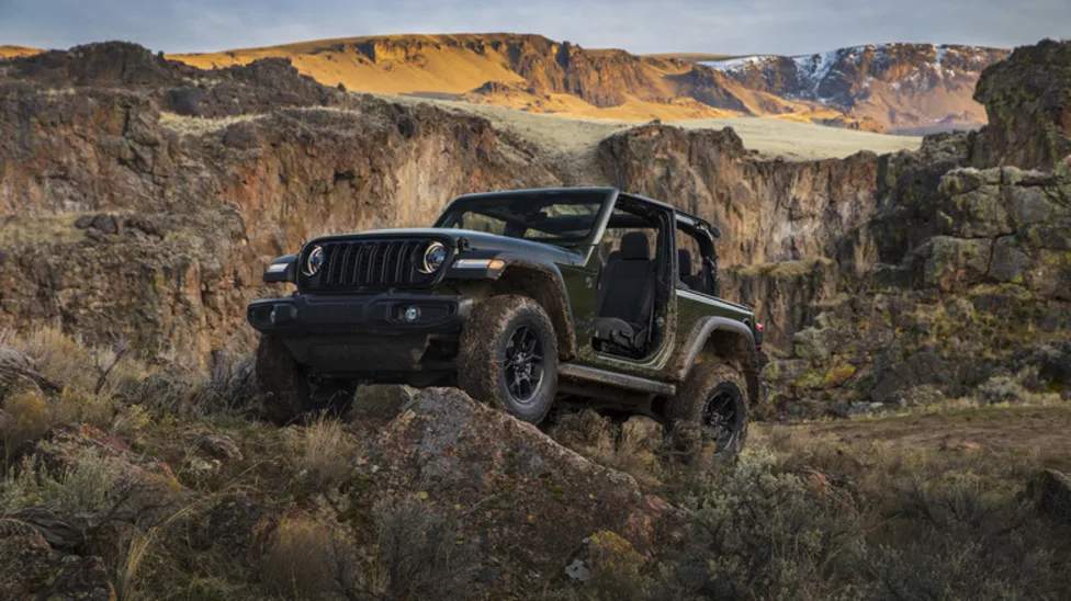 Mobil Jeep Wrangler berwarna merah melintasi jalur off-road berbatu.