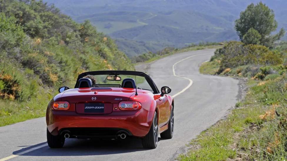 Mazda MX-5 Miata merah melaju di jalanan berliku pinggir pantai saat road trip